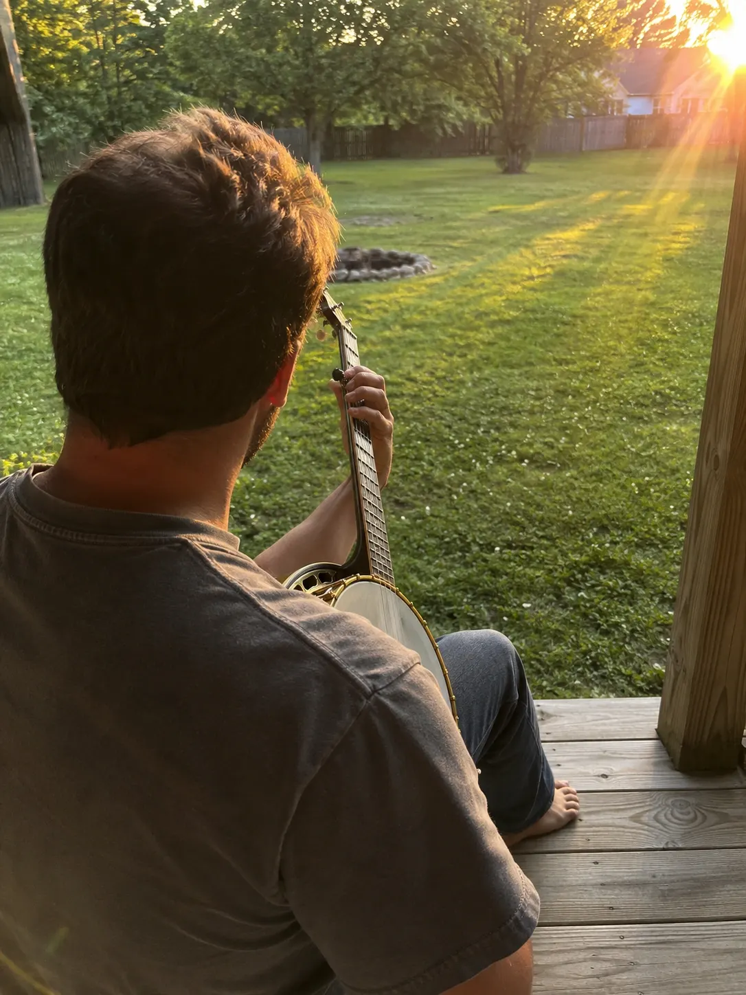 Player practicing clawhammer banjo on a porch at sunset